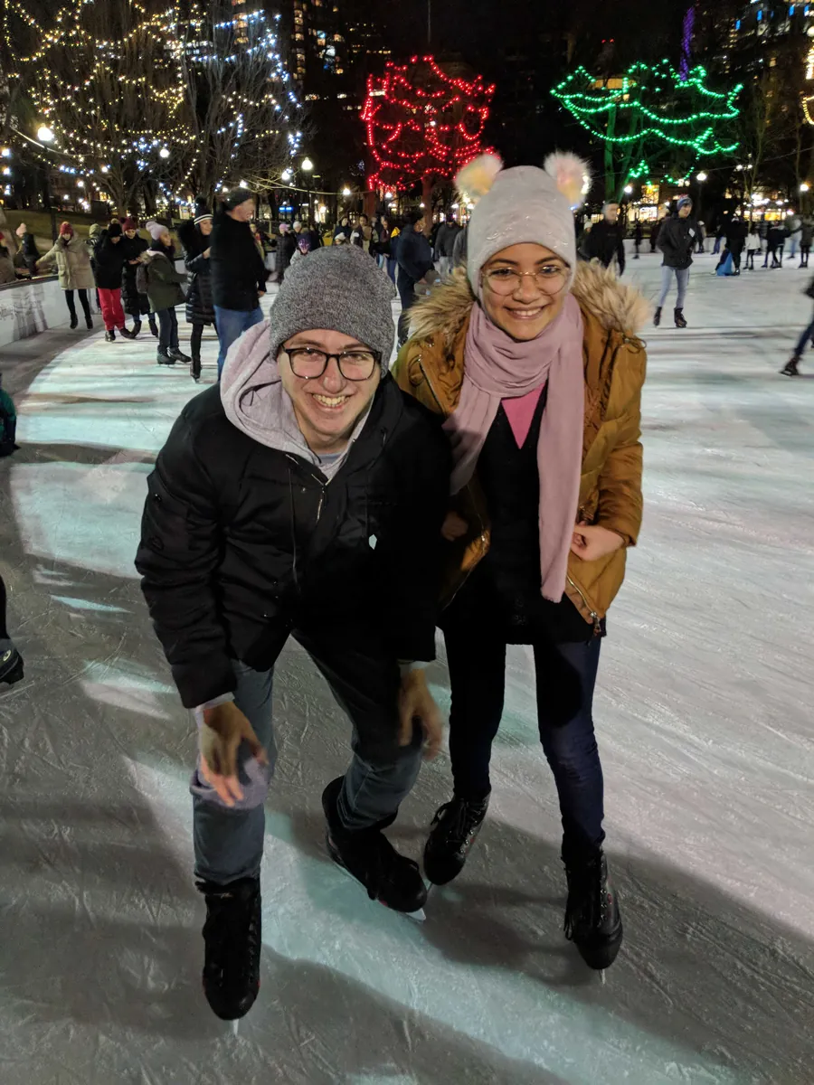 A couple laughing together while ice skating under string lights